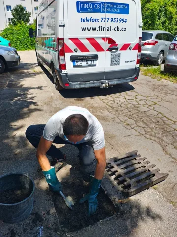 Technik ručně vybírá kal z odklopené uliční vpusti vedle vozu