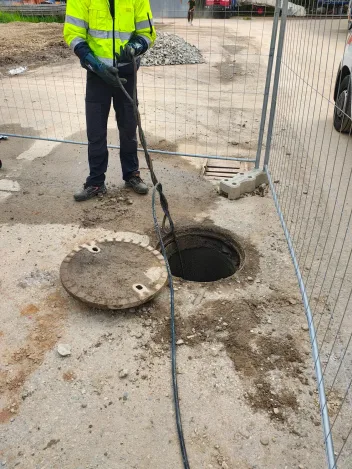 Technik v reflexní vestě proplachuje šachtu na oploceném staveništi