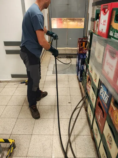 Tlaková hadice natažená prodejnou k&nbsp;odpadu mezi regály
