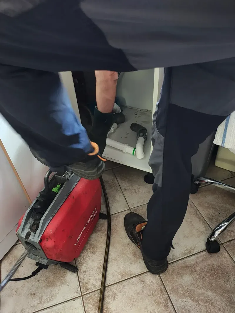 Technik čistí strojem odpad pod nerezovým dřezem v kuchyni provozovny