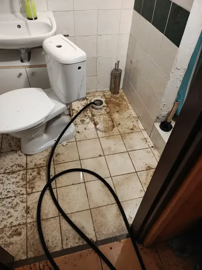Znečištěná dlažba na WC s&nbsp;nataženou hadicí před zásahem