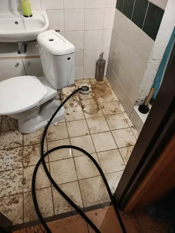 Zaplavená podlaha WC s nataženou hadicí před havarijním zásahem